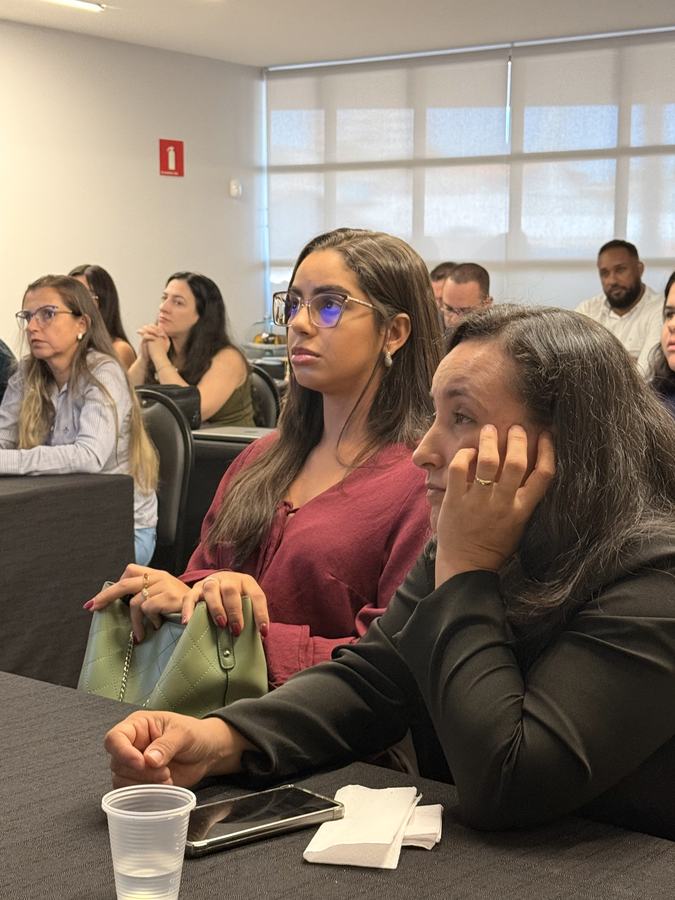Duas participantes acompanham atentamente a aula, sentadas próximas à janela da sala de treinamento.