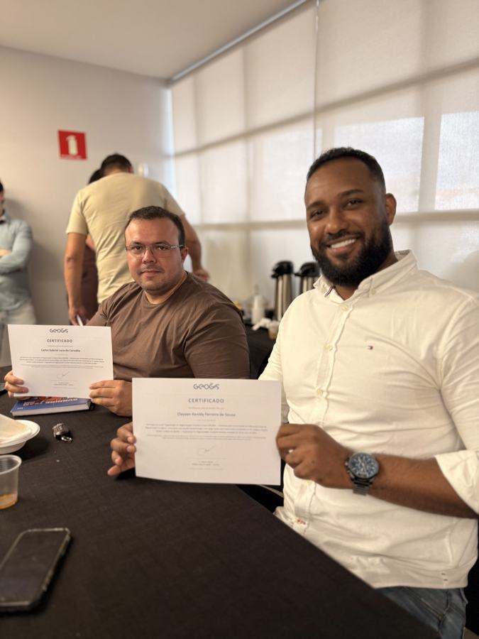 Dois participantes sorriem segurando os certificados de conclusão do curso.